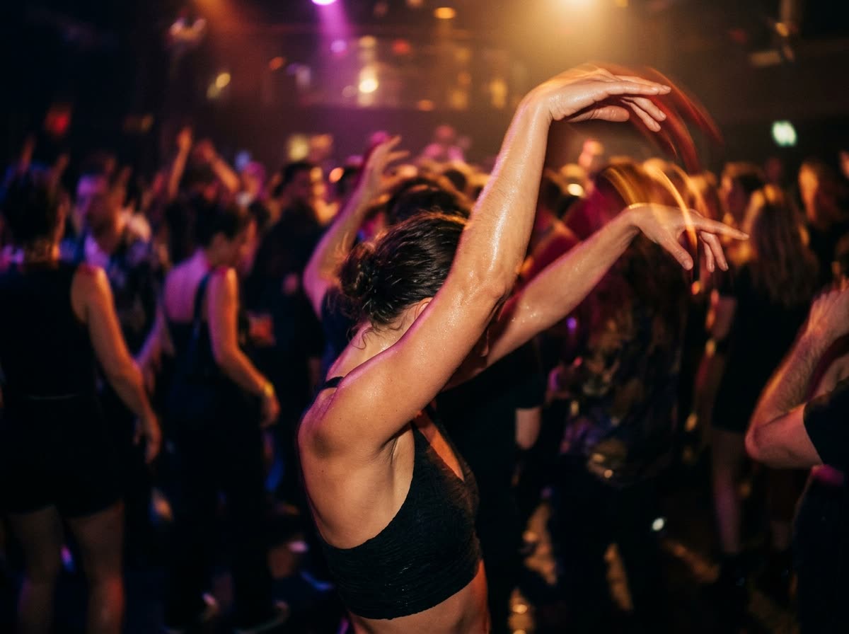 A dancer's raised arms and torso, cropped above the shoulders, on a crowded dance floor.